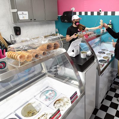 LOVELAND, CO - JANUARY 22, 2021:   Ariana Dodds, center right, hands and ice cream cone to customer Tom Buchanan, right, on Friday, Jan. 22, 2021, at her new ice cream shop, Ice Scream Ice Cream at 4221 W. Eisenhower Blvd. in the Former Esh's Grocery store building in west Loveland. Employee Cameo Blakeney, far left, prepares the rest of the order.    (Jenny Sparks/Loveland Reporter-Herald)