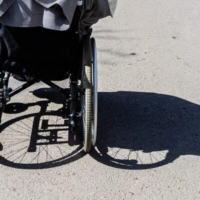 Shadow of the wheelchair and the tires. Shadow of a woman sitting on a wheelchair. Invisible women sitting in wheelchair is shadowed to right. Back of the wheelchair at outdoor shadowed to the right.